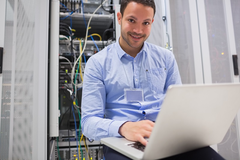 Happy man using laptop to check servers in data center
